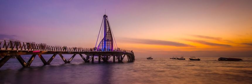 The illuminated Los Muertos Pier extending over the ocean during a vibrant golden sunset near Casa Dona Susana