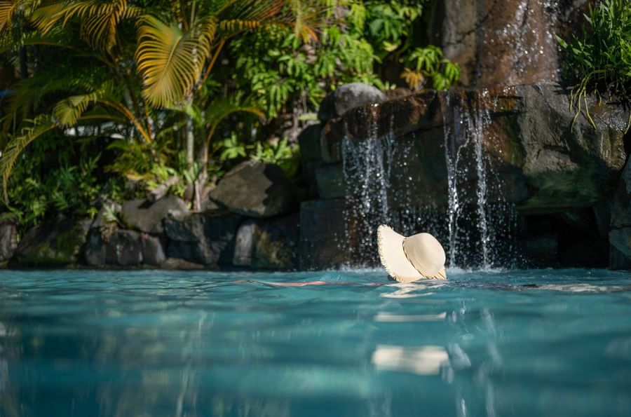 Swimmer wearing a sun hat floating in pool with waterfall at Tokatoka Resort.
