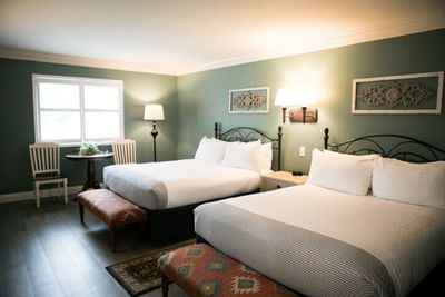 Two beds in a room with green walls, wooden floor, white pillows, and a small table with two chairs.