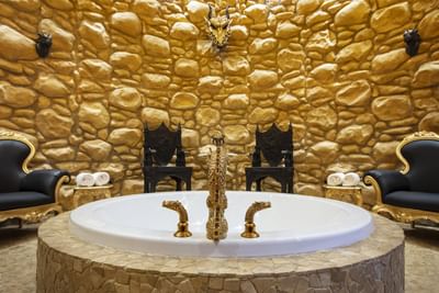 Crown of the Pendragons bathroom with a golden dragon faucet, a bathtub, and stone walls at The Roxbury