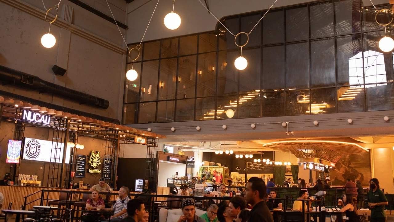 Spacious modern food hall with warm lighting, bar stalls, and customers near Camino Real Pedregal Mexico
