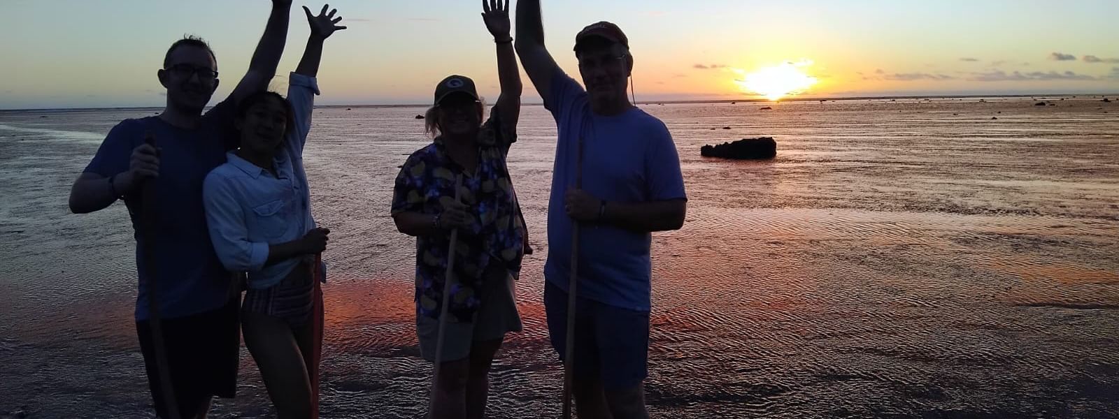Four tourists with sticks pose on the beach at sunset at Tambua Sands Beach Resort in Sigatoka