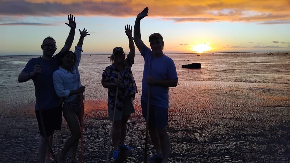 Four tourists with sticks pose on the beach at sunset at Tambua Sands Beach Resort in Sigatoka.