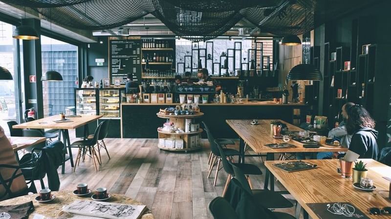 Interior of Newtown Restaurants with wood tables & black chairs under mesh ceiling at Novotel Sydney International Airport