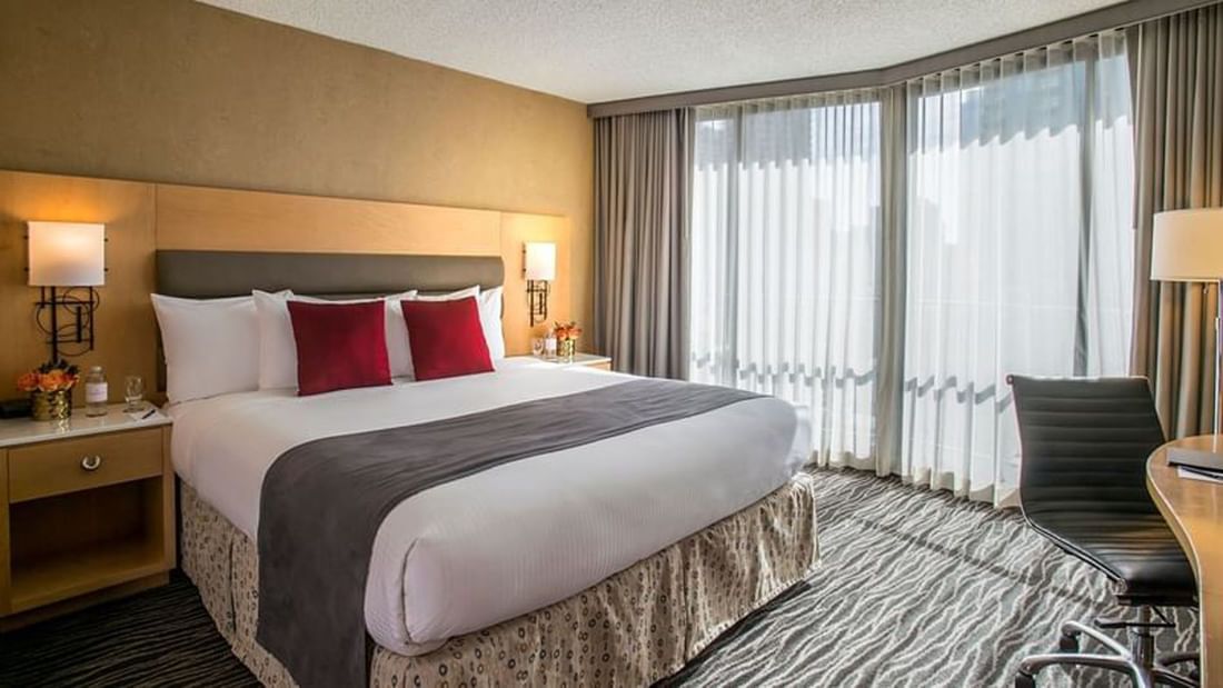 King bed with red pillows by large windows under soft light in Accessible Deluxe Rooms at Warwick Seattle