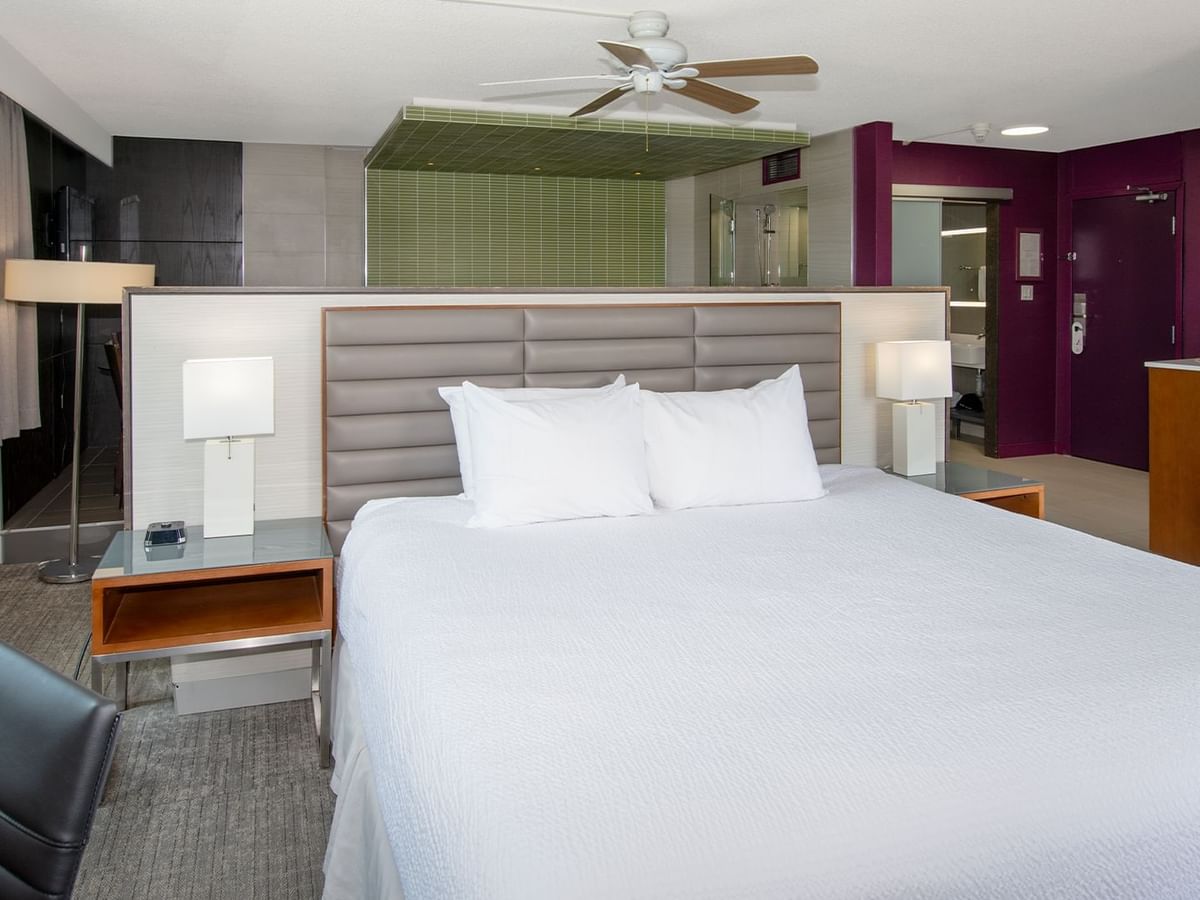 A hotel suite with a king bed, nightstands, a chair, and a ceiling fan.