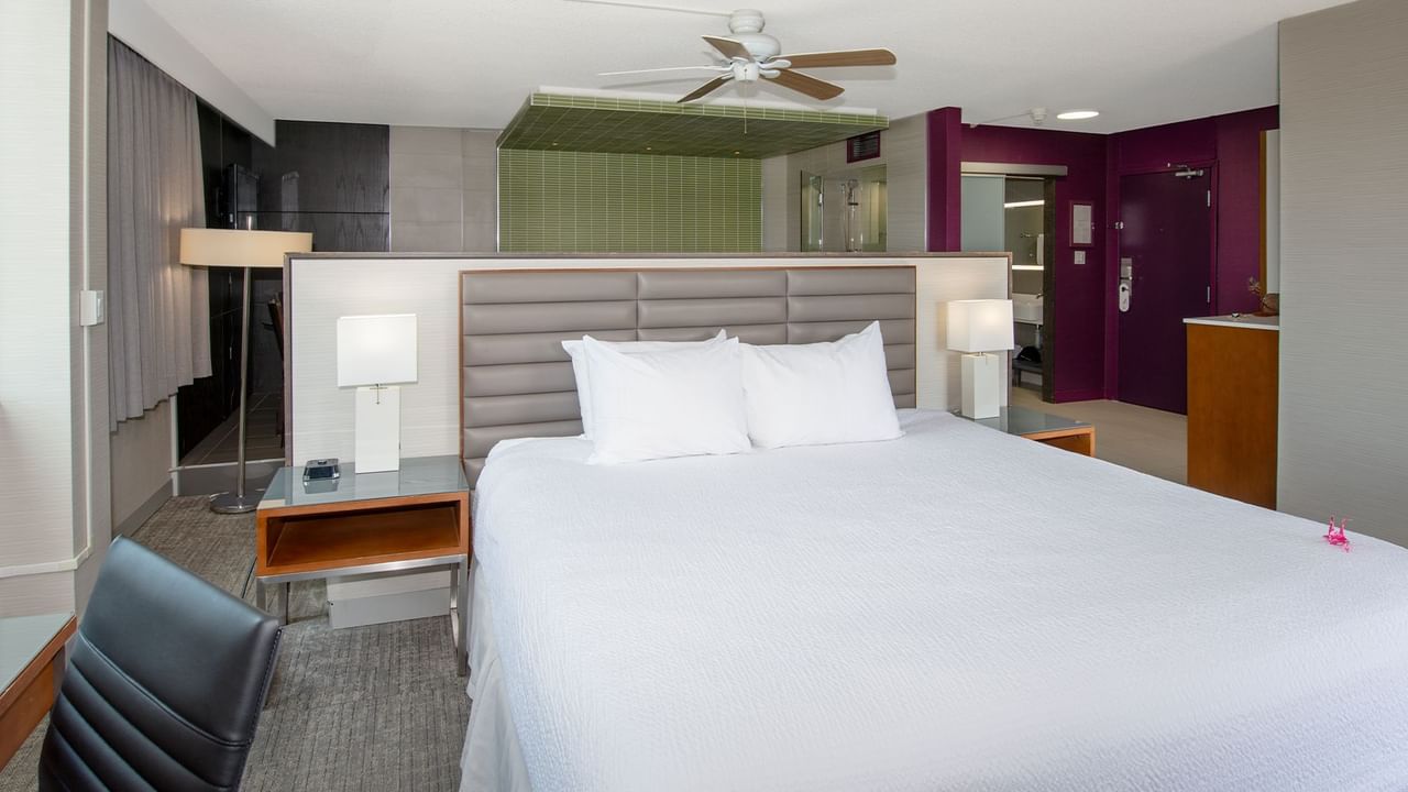 A hotel suite with a king bed, nightstands, a chair, and a ceiling fan.