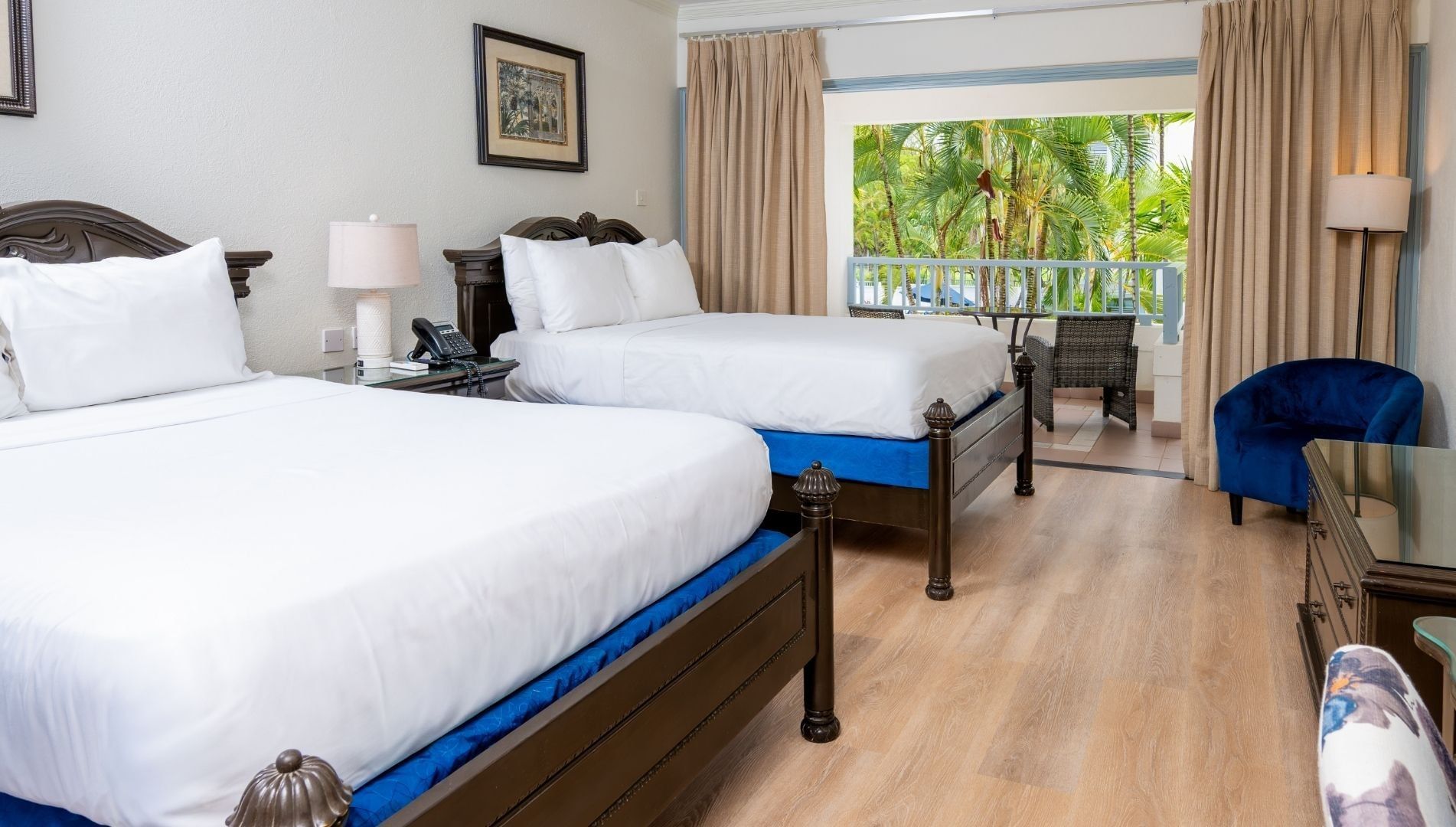 Two beds with decorative towel swans by a nightstand lamp under canvas art at Savannah Beach Hotel