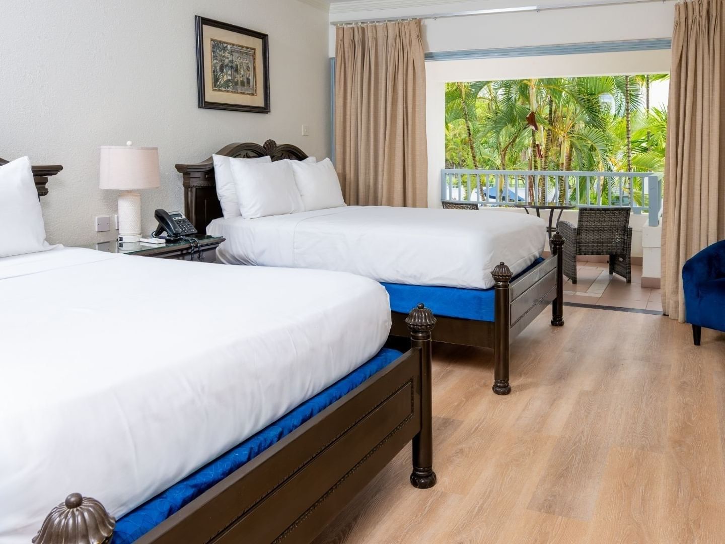 Two beds with white sheets and blue bases in a room with a balcony at Savannah Beach Hotel.