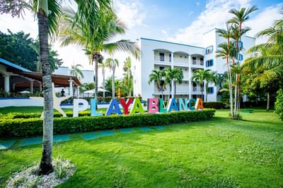 Colorful Playa Blanca sign on manicured lawn with palm trees and white resort buildings at Playa Blanca Beach Resort