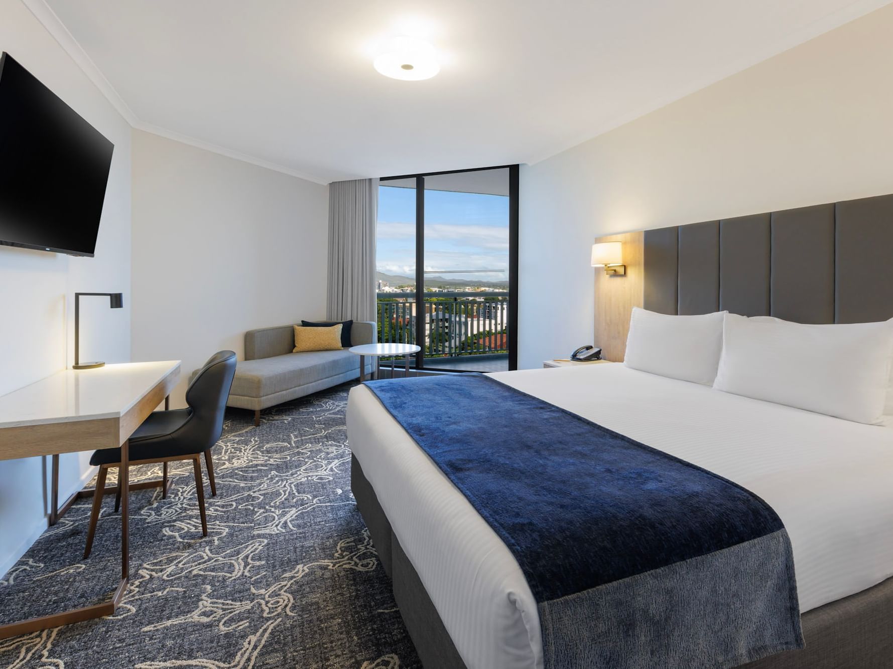 Modern King Room at Hotel Grand Chancellor Brisbane featuring a work desk, navy bed runner, and large window with views of the Brisbane CBD skyline.