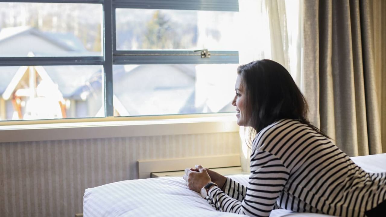 Woman lying on bed looking out a hotel window in Whistler