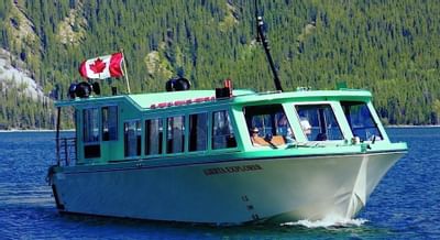 Alberta Explorer boat sailing on Lake Minnewanka, surrounded by lush green forest near Blackstone Mountain Lodge