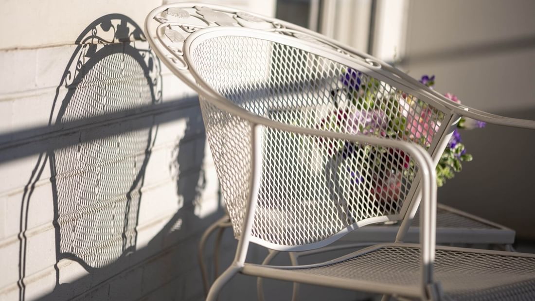 White metal chair by a brick wall under the sun on a private balcony in Classic Rooms at Warwick Denver