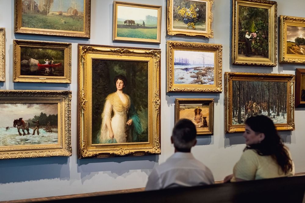 Two visitors admiring a gallery wall of ornate framed paintings at Warwick Le Crystal Montreal