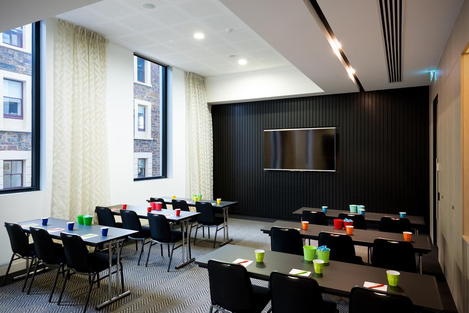 Classroom-style table set up facing wall-mounted TV in The Hub at Ibis Adelaide