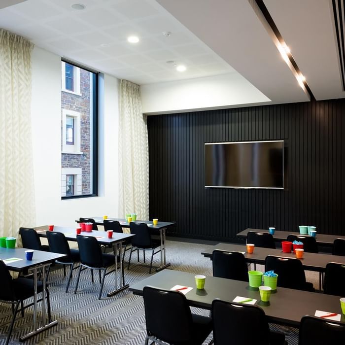 Classroom-style table set up facing wall-mounted TV in The Hub at Ibis Adelaide