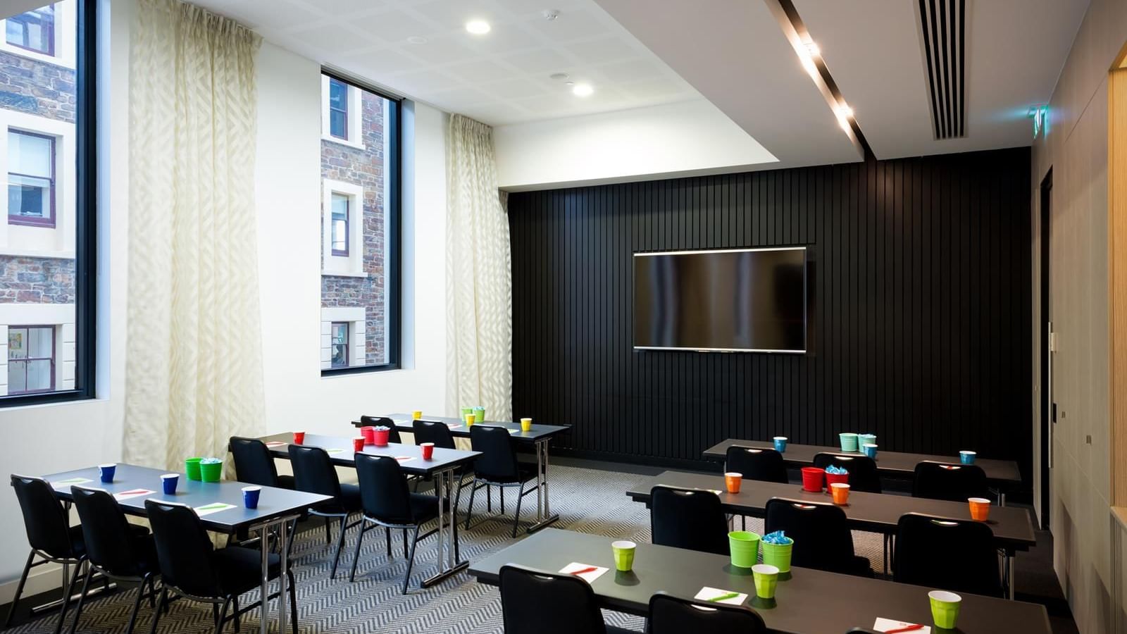 Classroom-style table set up facing wall-mounted TV in The Hub at Ibis Adelaide