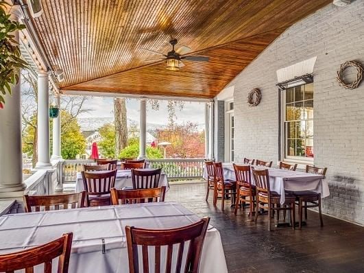 Dining tables with linens by wooden chairs, under a beadboard porch ceiling near mountain views at Simsbury 1820 House