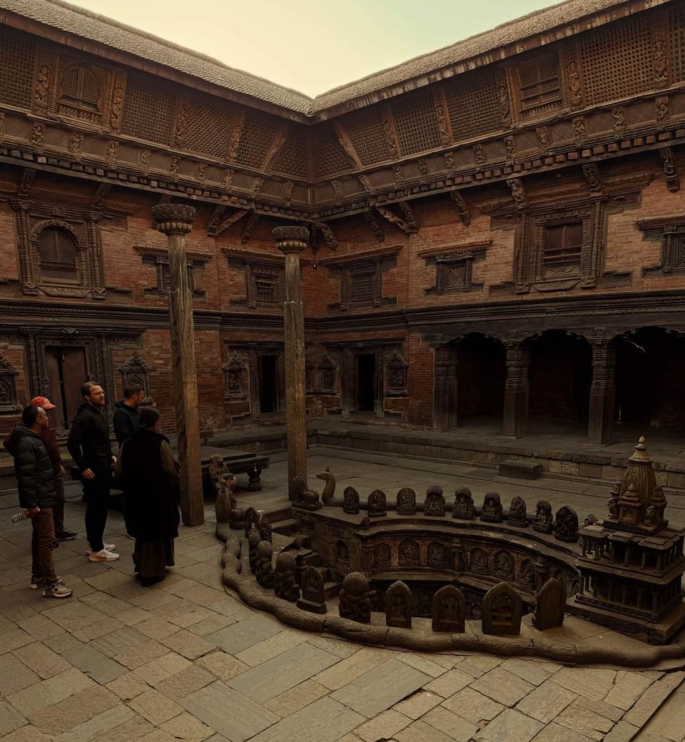 An area with wooden architecture, stone carvings, & sunken structure surrounded by visitors at Dwarika's Hotel Kathmandu