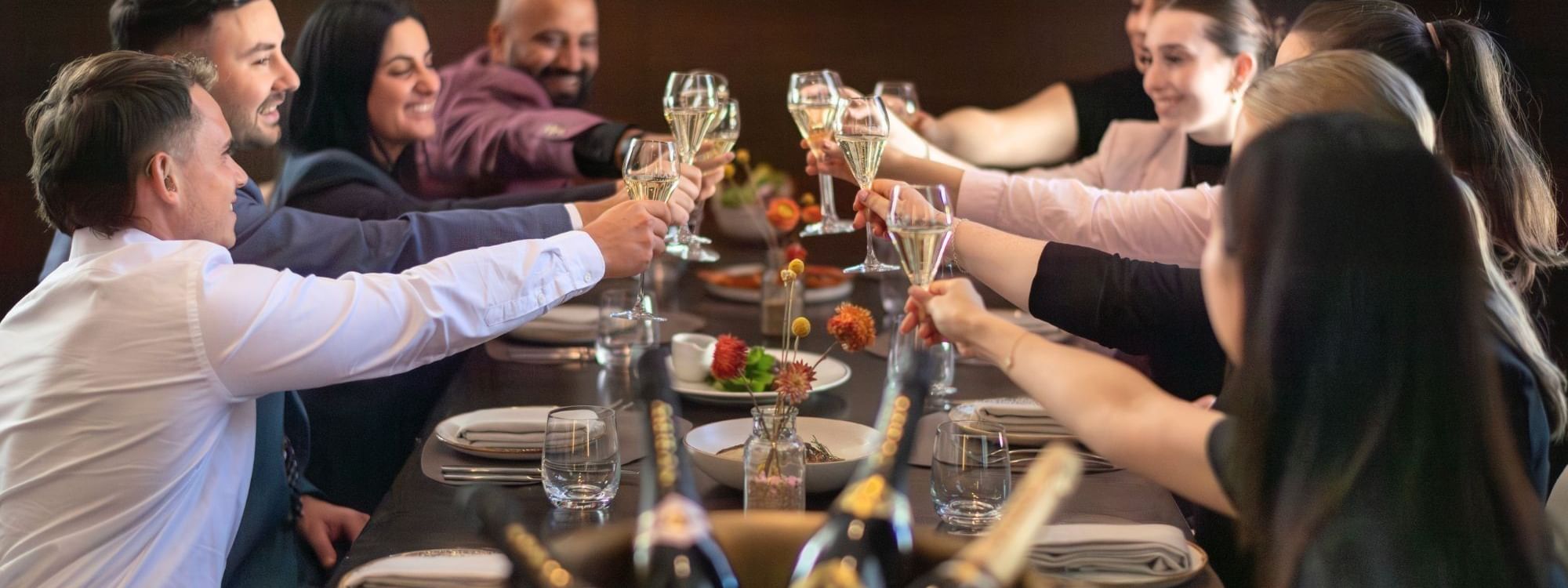 Group of friends toasting with champagne glasses at an elegant dinner table with framed artwork on the wall behind them