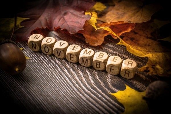 The word November spelled out in small wooden beads surrounded by fall leaves.