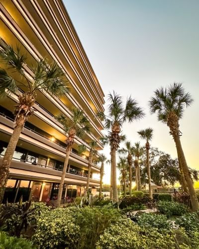 The exterior of a 9-story hotel building with palm trees and tropical landscaping at sunset. Rosen Inn at Pointe Orlando is a great place to stay for Galentine's Day in Orlando.