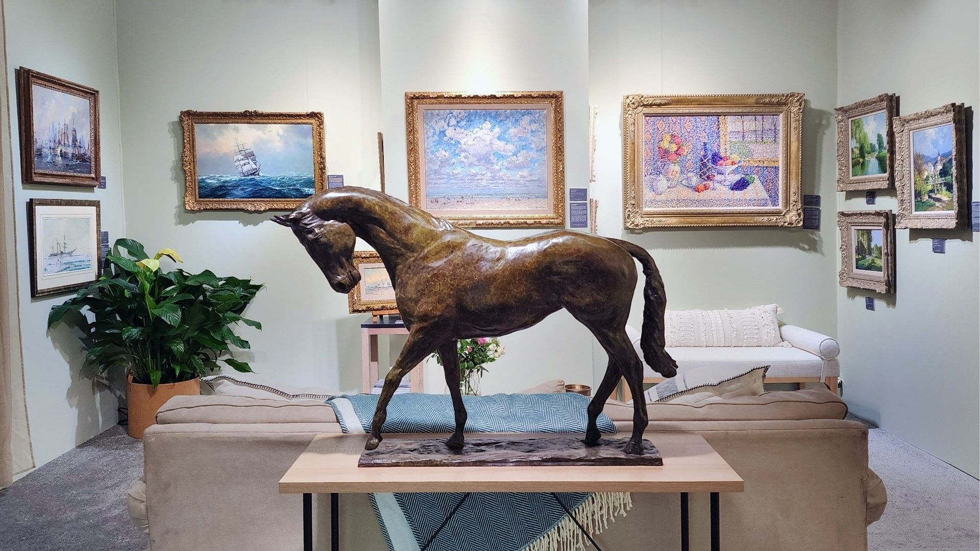 Bronze horse sculpture displayed in a cozy room with art frames and couches.