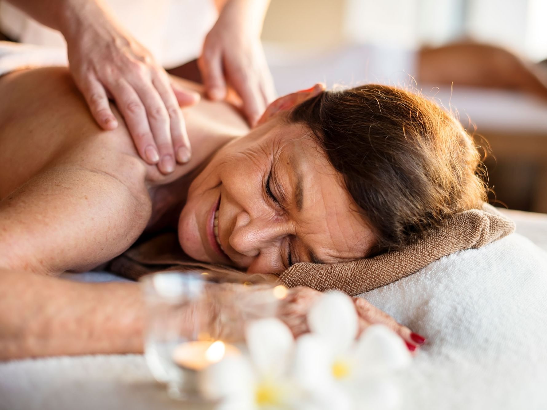 Woman in spa receiving shoulder massage with candles and flowers nearby.