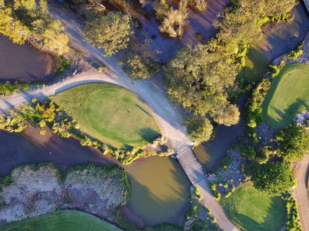Aerial view of a golf course with paths, ponds, and lush greenery.
