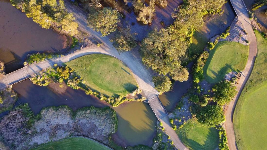 Aerial view of a golf course with paths, ponds, and lush greenery.