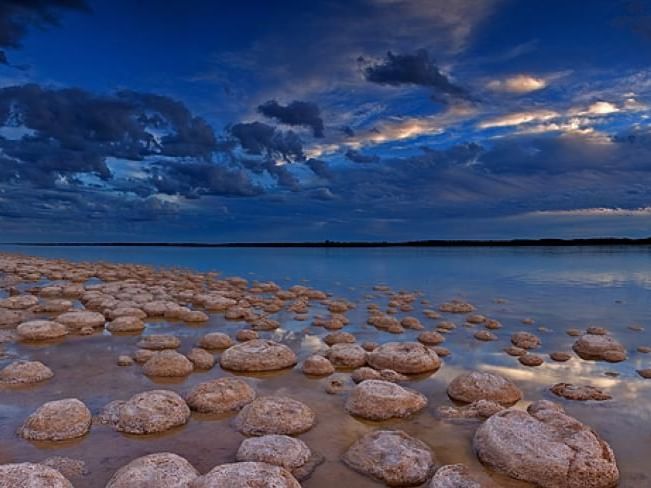 Scenic view of a vast lake with round rocks and dramatic sky at Stromatolites and Lake Clifton near The Sebel Mandurah