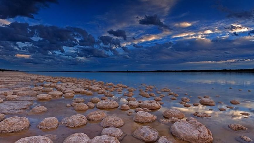 Scenic view of a vast lake with round rocks and dramatic sky at Stromatolites and Lake Clifton near The Sebel Mandurah