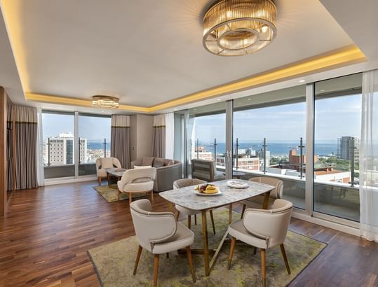 Titanic Port Bakırköy'de, şık mobilyalar ve dekoratif öğelerle donatılmış, yemek alanı, geniş pencereler ve şehir manzarası sunan Suite odada modern oturma alanı.