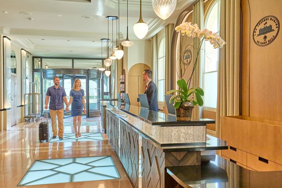 Couple with luggage arrives at the elegant hotel reception desk to check in at Le Grand Hôtel des Thermes