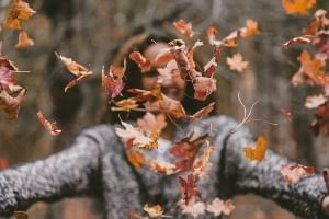 A woman throwing fall leaves in to the air on Thanksgiving. 