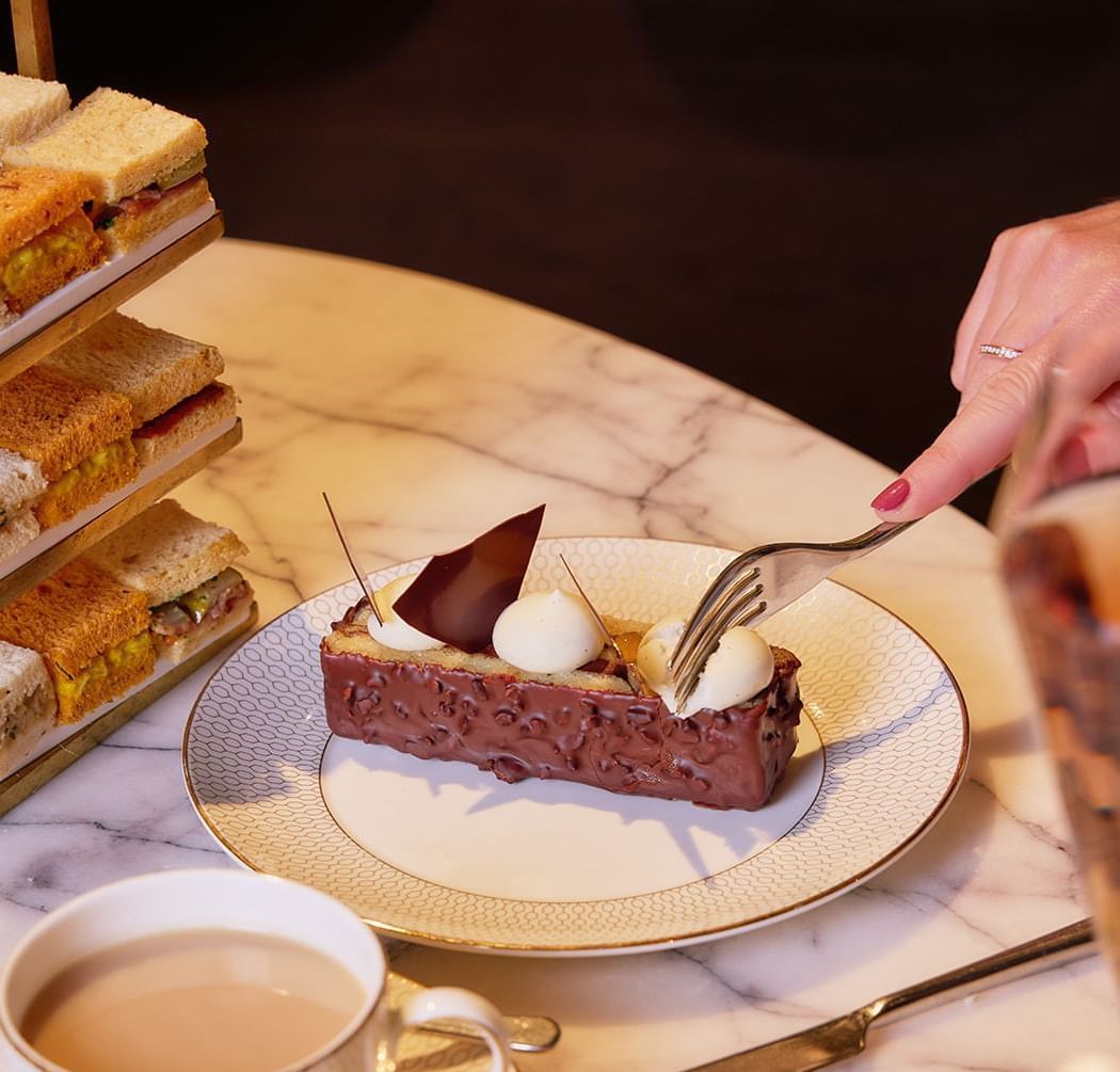 A hand taking a bite of a rich chocolate dessert during an afternoon tea at The Londoner Hotel
