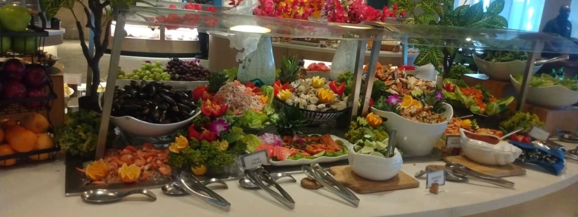 Buffet table with assorted fruits, salads, and seafood, topped with utensils and decorative flowers