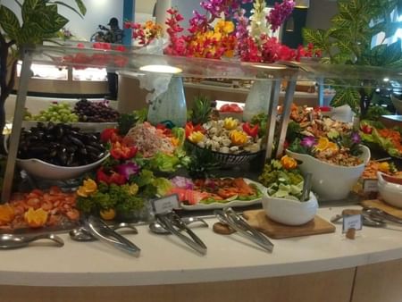 A buffet table displays an assortment of fruits, salads, and seafood under a glass cover.