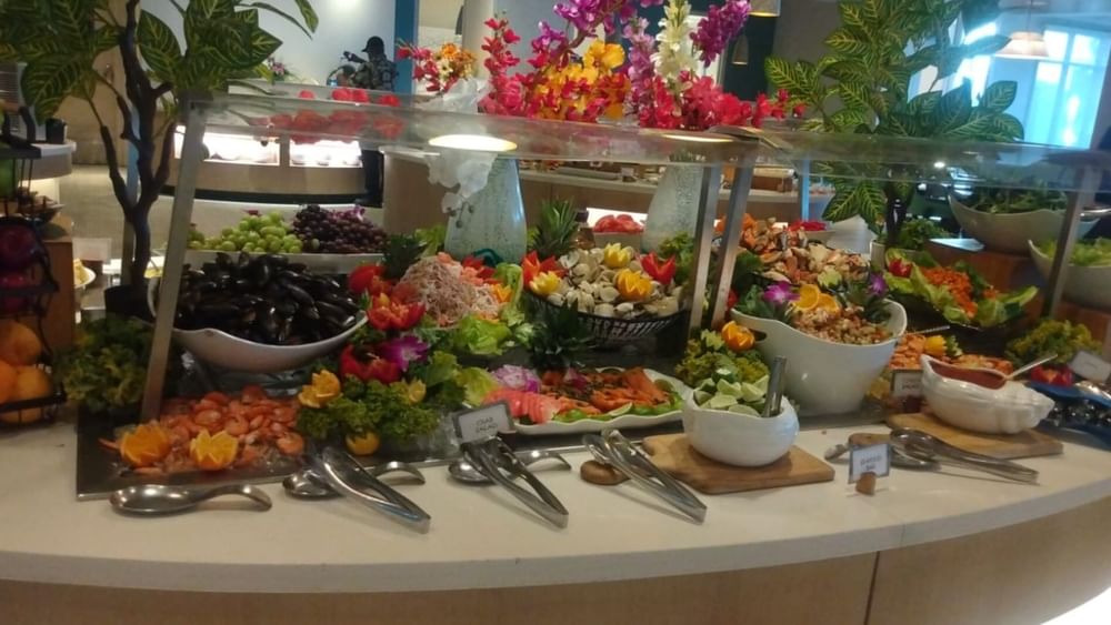 Buffet table with assorted fruits, salads, and seafood, topped with utensils and decorative flowers