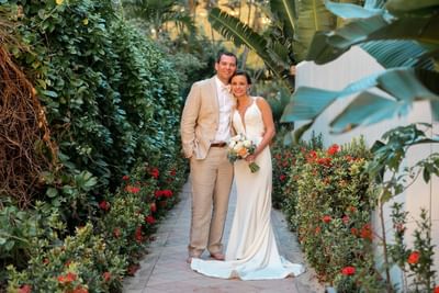 Bride and groom standing together on a tiled walkway lined with lush green tropical plants at Emerald Beach Resort