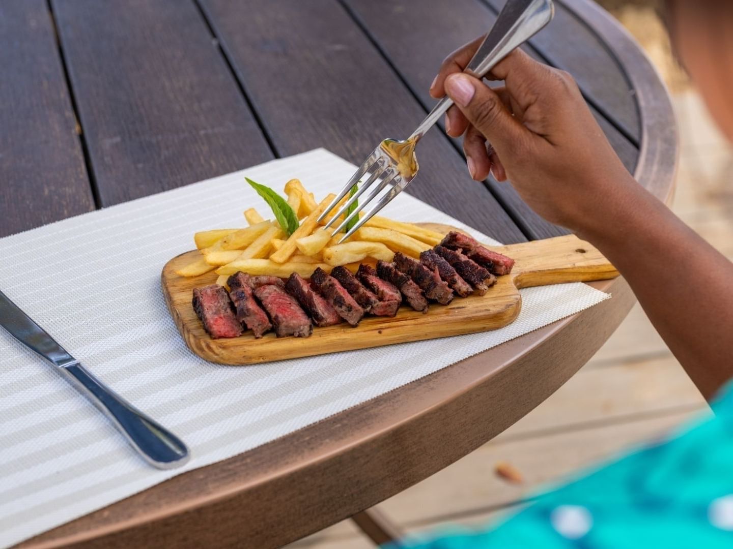 Woman holding a fork over a steak and fries at Savannah Beach Hotel.
