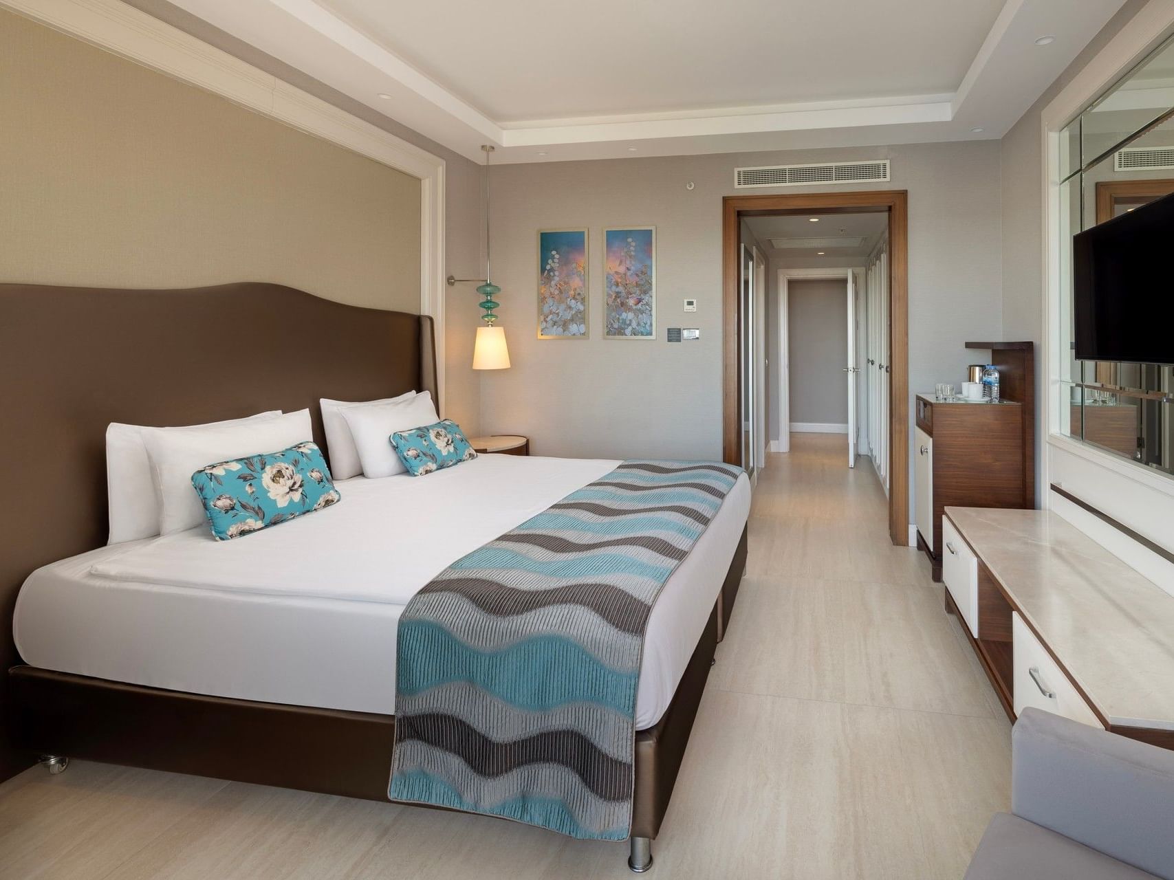 Modern hotel room with king bed, turquoise accent pillows, flat-screen TV, and light wood flooring at Titanic Deluxe Golf Belek