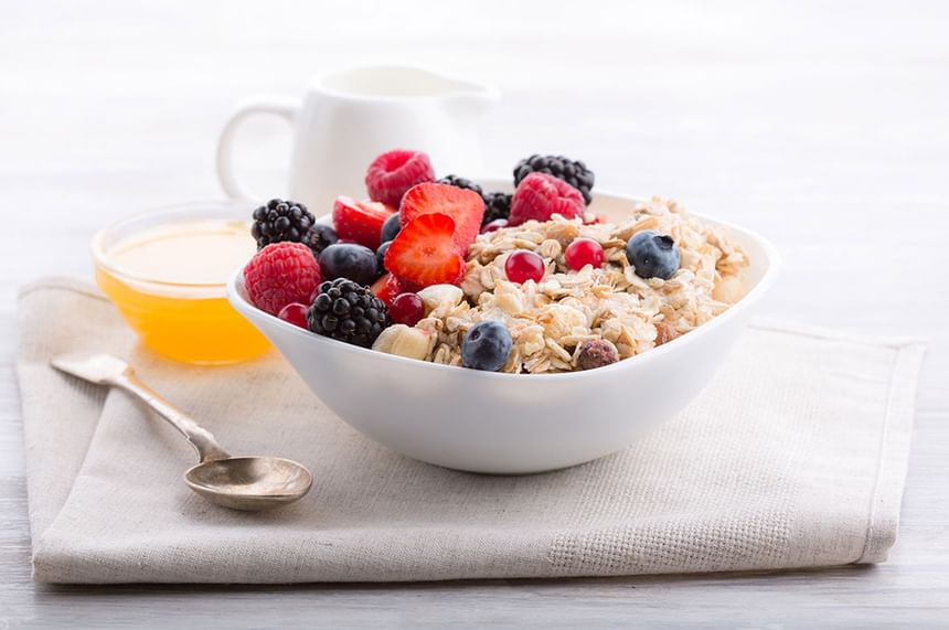 Close-up of bowl of granola topped with fresh berries & banana with honey and a cream pitcher in Restaurant at D Sabana Hotel