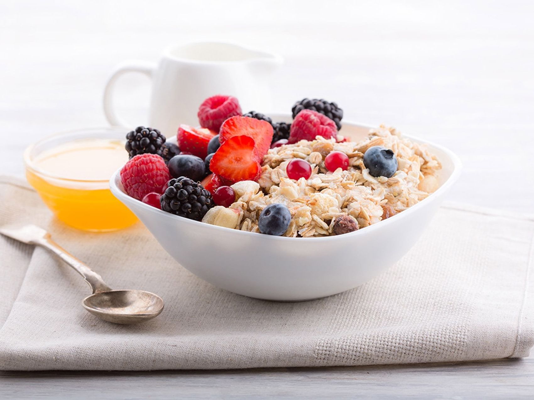 Close-up of bowl of granola topped with fresh berries & banana with honey & cream pitcher in Restaurant at D Sabana Hotel