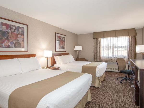 A hotel room with two queen beds, a desk with a TV, and a window with curtains.
