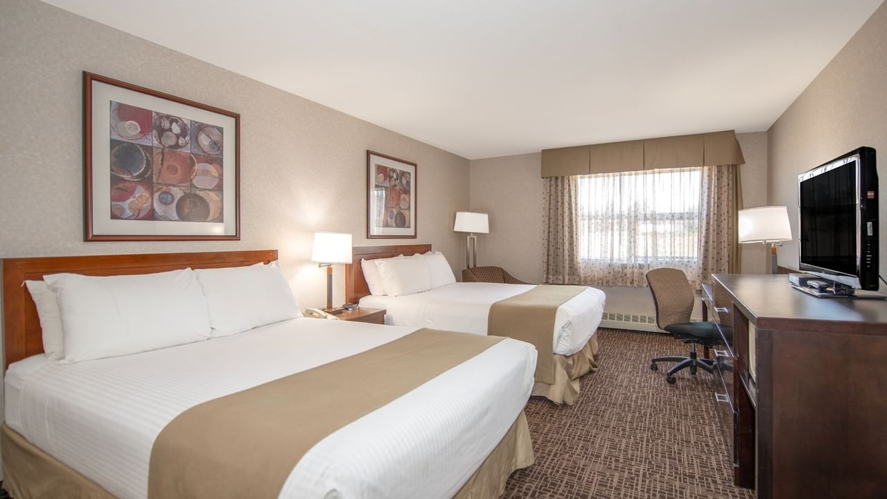 A hotel room with two queen beds, a desk with a TV, and a window with curtains.