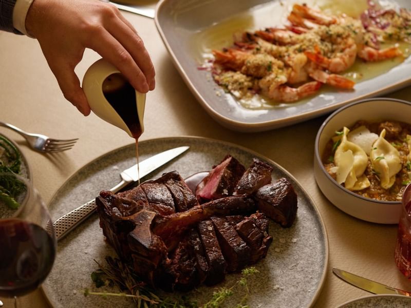Hand pouring sauce on steak with prawns & pasta in Modo Mio at Crown Promenade Perth