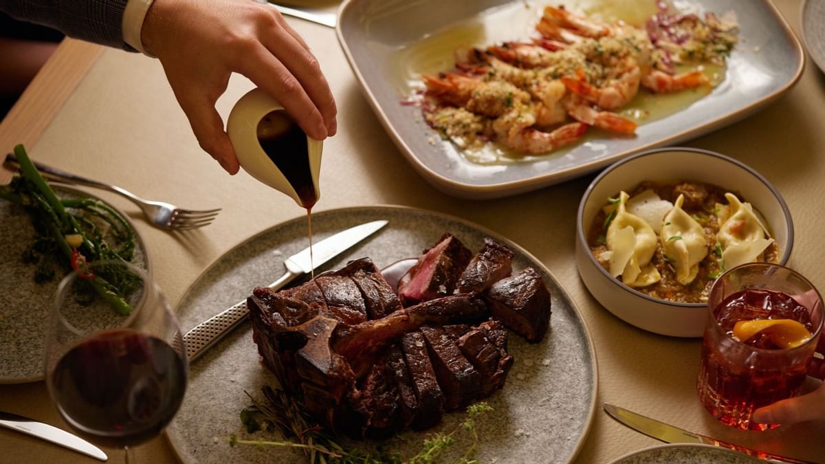 Hand pouring sauce on steak with prawns & pasta in Modo Mio at Crown Promenade Perth