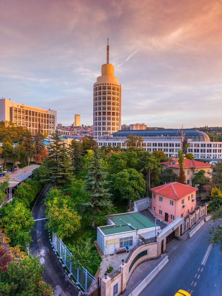 City view with a tall white tower by green trees, under a sunset sky in Ankara near Warwick Hotels & Resort